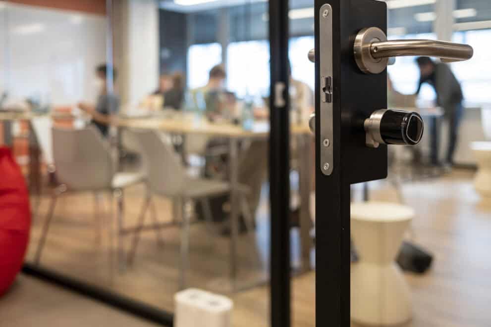 Close up of ajar glass office door focusing on the lock with blurred office background.